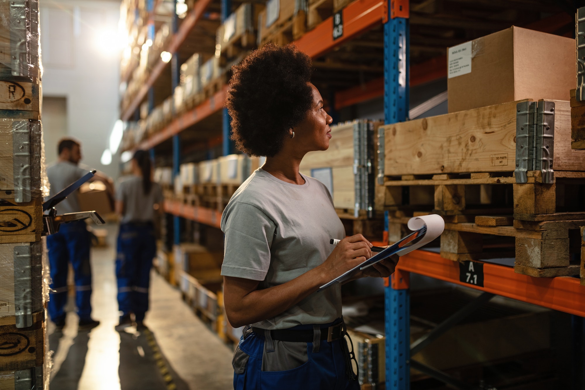 African American worker taking notes while checking stock in a warehouse.